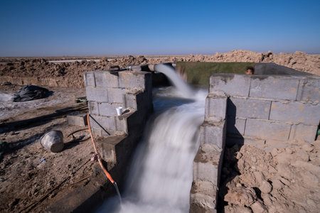 A water channel flowing from a concrete structure in a dry landscape, with clear blue skyのeditorial素材