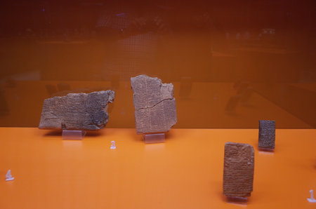 Ancient clay tablets displayed in a museum, featuring cuneiform writing, on an orange backgroundのeditorial素材