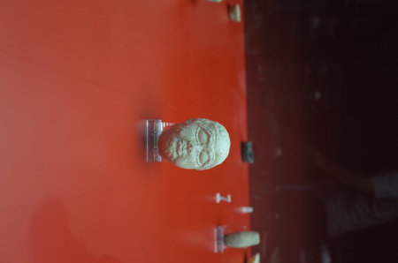 A small ancient stone sculpture resembling a human head, displayed on a red surface, with a blurred...