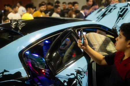 A crowd gathered around a modified car with vibrant blue and black design, a child taking a photo...