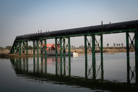 Industrial Pipeline Structure Crossing the Wide River Channel, Supported by Green Metal Trestles, Reflecting Modern Infrastructure on the Water.の写真素材