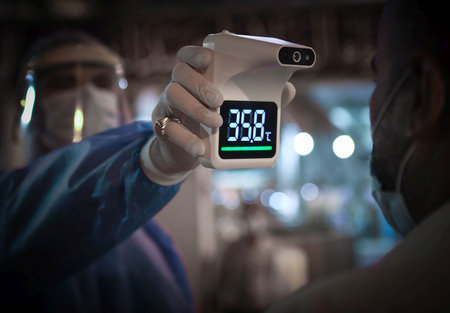 A healthcare worker measuring temperature with a digital thermometer, wearing protective gear, in a...