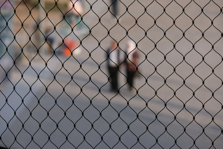 A blurred view of two people walking behind a netted fenceの写真素材