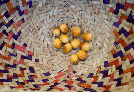 A woven basket with a colorful pattern containing several small yellowish eggs or fruitsの写真素材