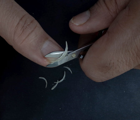 A person using scissors to trim small pieces of material from their finger, with shavings visible on...
