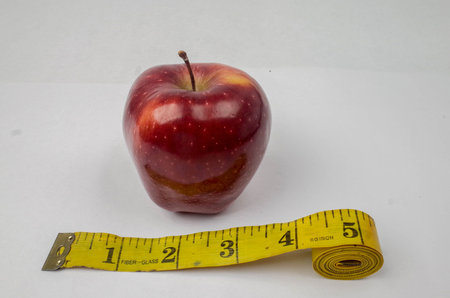 A red apple placed next to a measuring tape on a white background