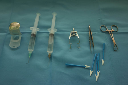 A collection of medical instruments arranged on a blue surgical cloth, including syringes, forceps,...