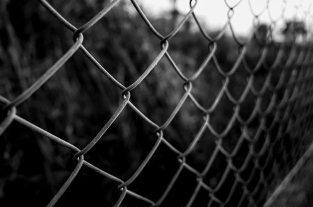 Black-and-white close-up of a chain-link fence with shallow depth of field, diagonal perspective, blurred backgroundの写真素材