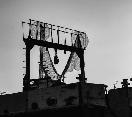 Silhouetted industrial ship gantry with netting and winch against a clear sky, high-contrast black-and-white compositionの写真素材