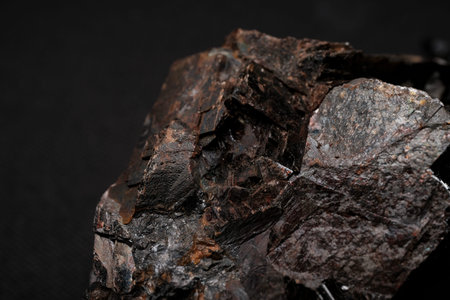Close-up of dark brown metallic rock with angular crystalline surfaces against a black background