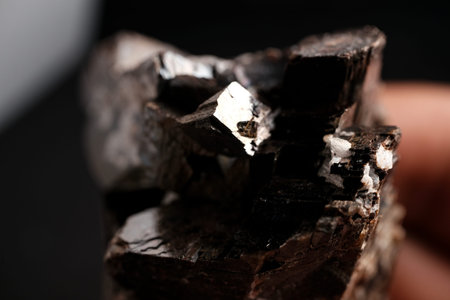 Close-up of a dark metallic, crystalline mineral with glossy reflective faces against a black background, showing blocky geometric structure and brownish highlights.の写真素材