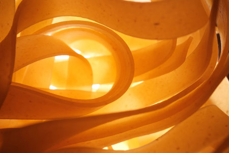 Warm abstract close-up of curled wooden or paper strips backlit with golden light, organic flowing...