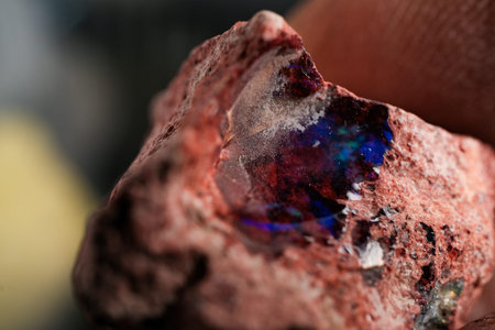 Macro shot of rough opal embedded in red matrix, showing vivid blue and purple play-of-color,...