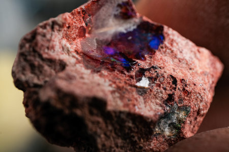 Rough reddish rock with vibrant blue-purple opal-like patch, macro close-up showing texture and...