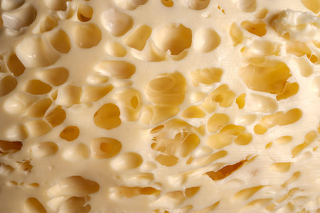 Macro close-up of pale yellow cheese with irregular holes and creamy texture, warm lighting