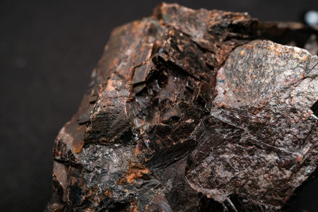 Close-up of a dark, metallic iron ore rock with rusty brown patches and flaky texture on a black...
