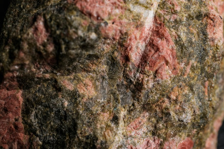 Close-up macro of a textured rock surface with pink and green mineral veins, rough crystalline...