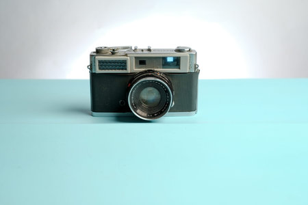 Vintage rangefinder film camera centered on pastel blue surface with white background, minimal...