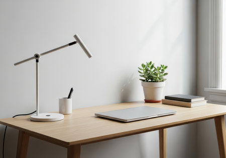 Minimalist workspace with closed laptop, lamp, plant, and books on wooden deskの素材
