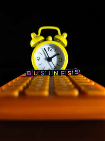 Selective focus.A yellow clock and calculator with word BUSINESS on a colorful dice with black background.Business concept.の写真素材