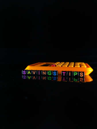 Selective focus.Word SAVINGS TIPS on a black dice with calculator and black background.の写真素材