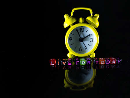 Selective focus.A yellow clock and word LIVE FOR TODAY on a black dice with reflection on a black background.の写真素材