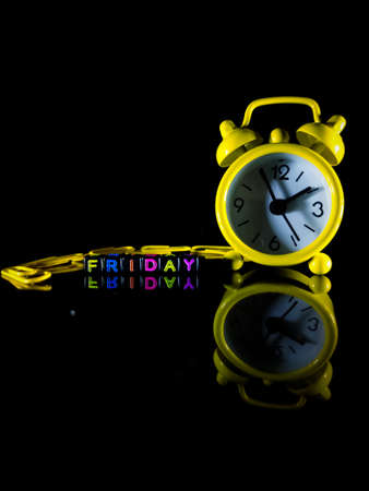 Selective focus.Word FRIDAY from black dice with yellow clock and reflection on a black background.Shot were noise and film grain.の写真素材