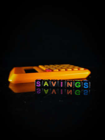 Selective focus.Word SAVINGS with reflection and calculator on a black background.Shot were noise and film grain.の写真素材