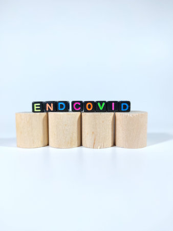 Selective focus.Word END COVID from black dice on a block cylinder with white background.Shot were...