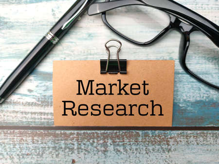 Pen,glasses and brown card written with text Market Research on wooden background. Business concept.の写真素材