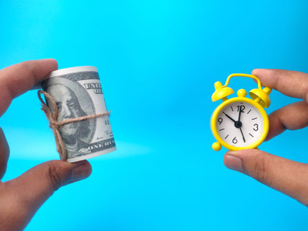Hand holding yellow alarm clock on a blue background with copy space.