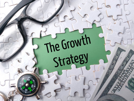 Top view glasses,compass and banknotes with text The Growth Strategy on a white puzzle backgroundの写真素材
