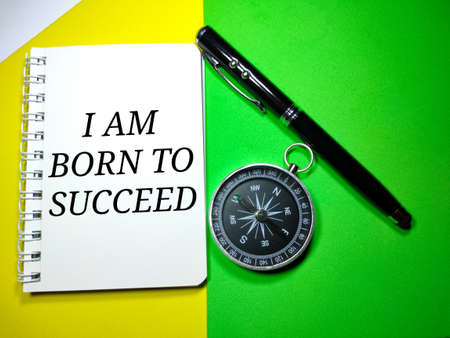 Selective focus.Word I AM BORN TO SUCCEED on a notebook with pen and compass on a yellow and green background.Motivation concept.Shot were noise and grain.の写真素材