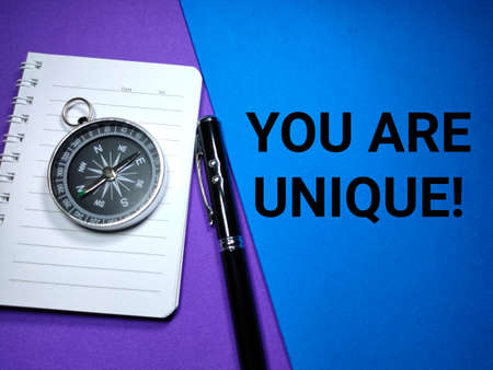 Selective focus.Compass on a notebook with pen and word YOU ARE UNIQUE on a colorful background.Shot were noise and grain.の写真素材