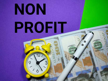Selective focus.Pen,clock and banknote with word NON PROFIT on a purple and green background.Business concept,shot were noise and grain.の写真素材