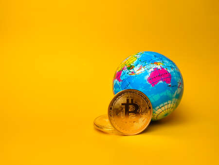 Bitcoins and world globe on a yellow background with copy space.の写真素材