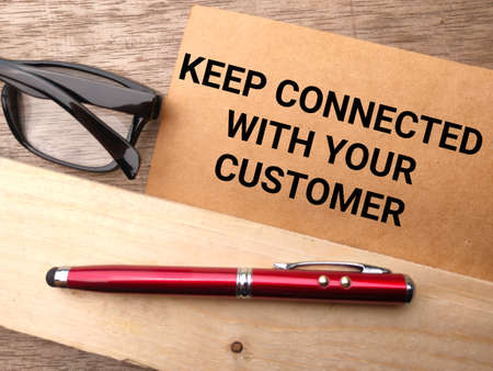 Glasses and pen with text KEEP CONNECTED WITH YOUR CUSTOMER on a wooden background.の写真素材