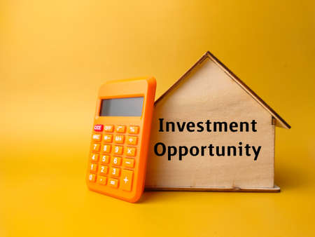 Wooden house and calculator with text Investment Oppurtunity on a yellow background.の写真素材