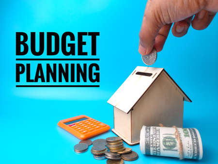 Hand putting money banknote into wooden house tubes with text BUDGET PLANNING.の写真素材