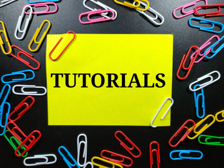 Text TUTORIALS on color note paper with paper clips on black background.
