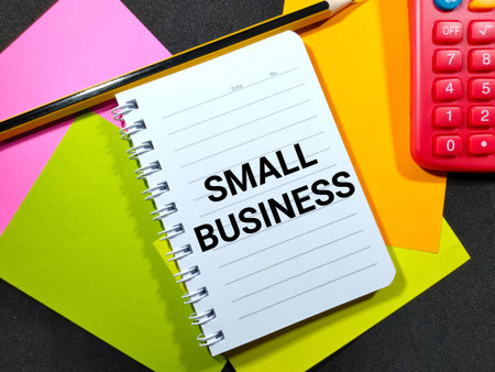 Word SMALL BUSINESS on notebook with pencil and calculator on black and colorful paper...
