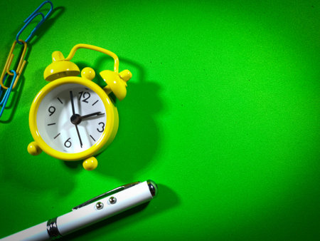 Selective focus of pen,clock and notebook on green background with copy space.