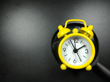 Selective focus of clock and magnifying glass on black background with copy space.