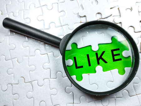 Selective focus.Word LIKE with magnifying glass and jigsaw puzzle on green background.の写真素材