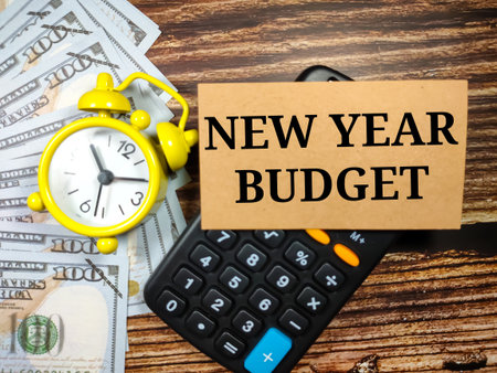 Business concept.Text NEW YEAR BUDGET with clock, banknote and calculator on a brown wooden...