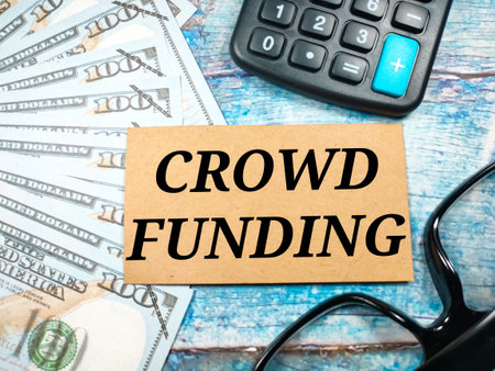 Business concept.Text CROWD FUNDING with banknote,calculator and glasses on wooden background.の写真素材