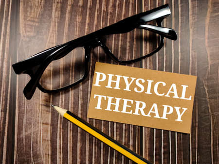 Medical concept.Text PHYSICAL THERAPY with glasses and pencil on a brown wooden background.の写真素材