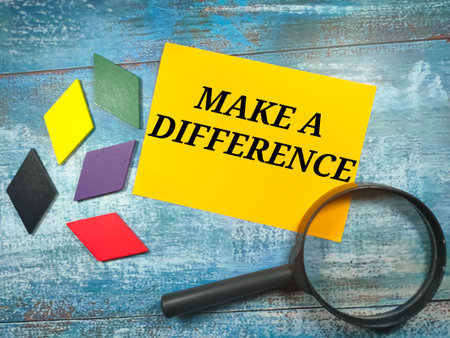 Text MAKE A DIFFERENCE with magnifying glass and colorful wooden jigsaw on blue wooden background.の写真素材