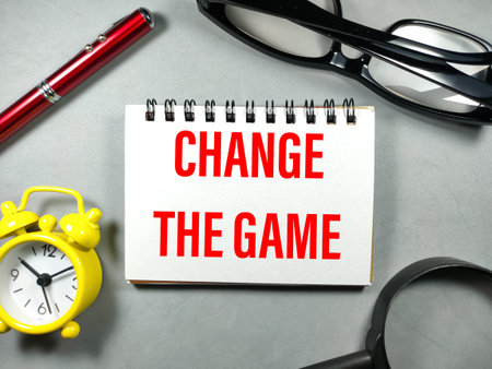 Business concept.Text CHANGE THE GAME with clock,pen,glasses and magnifying glass on gray background.の写真素材