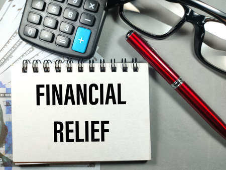 Business concept.Text FINANCIAL RELIEF with pen,glasses,banknote and calculator on gray background.の写真素材